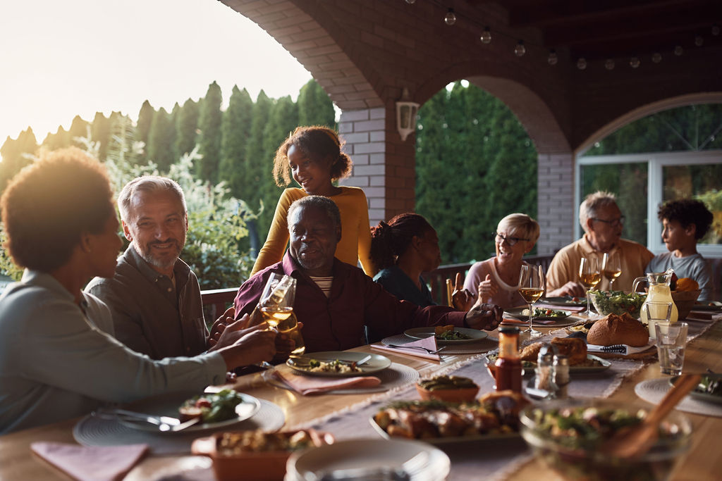 Three generations of a family sharing a meal at a long outdoor table at sunset
